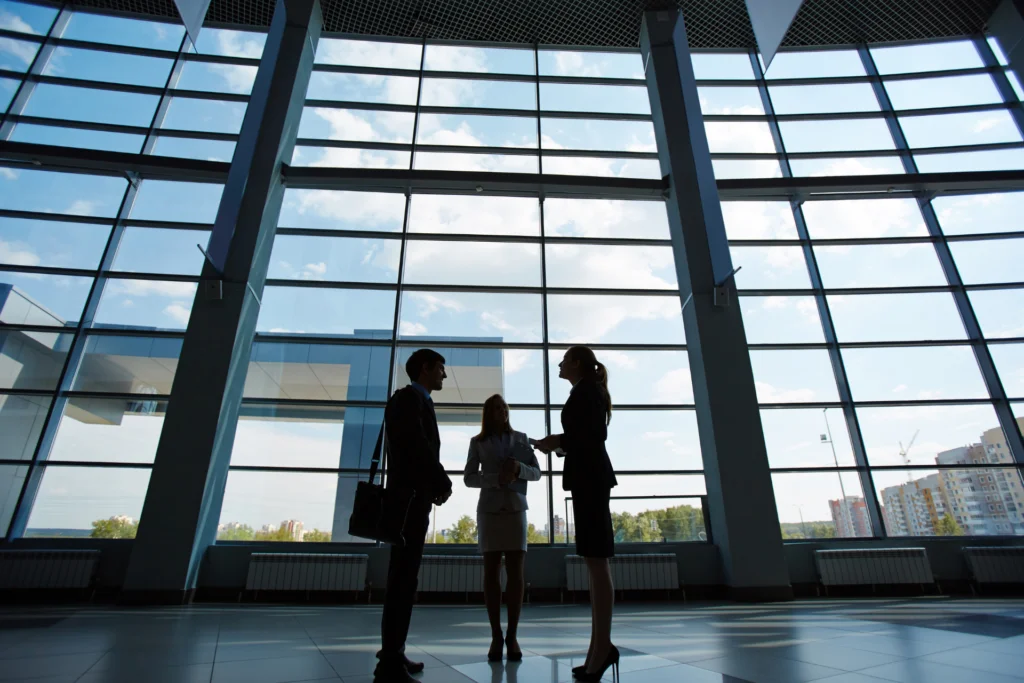 Three business professionals having a discussion in a modern office with large windows.